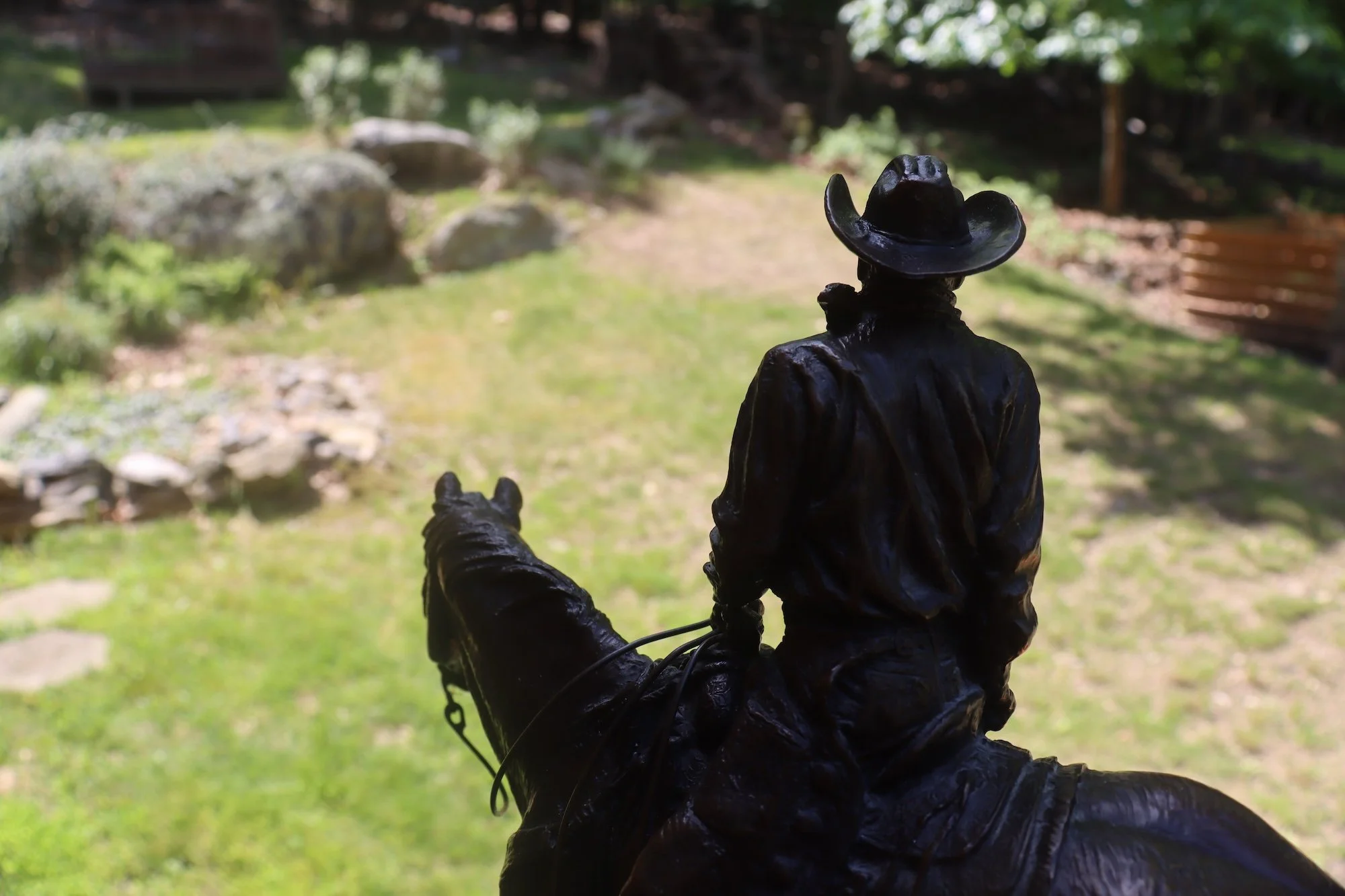 The bronze Wrangler statue, or Western Heritage Award, from the National Cowboy & Western Heritage Museum. Depicts a cowboy riding a horse, seen from behind, with trees and rocks in the background.