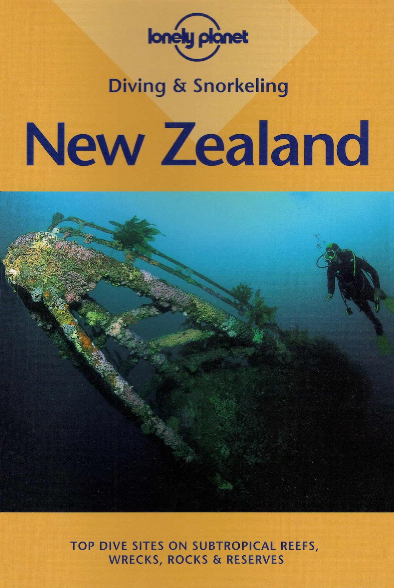 The cover of Lonely Planet's diving & snorkeling guide to New Zealand. A diver exploring a coral reef beside a rusted, wrecked shipwreck. The diver is wearing a wetsuit and snorkeling gear, surrounded by clear blue water.