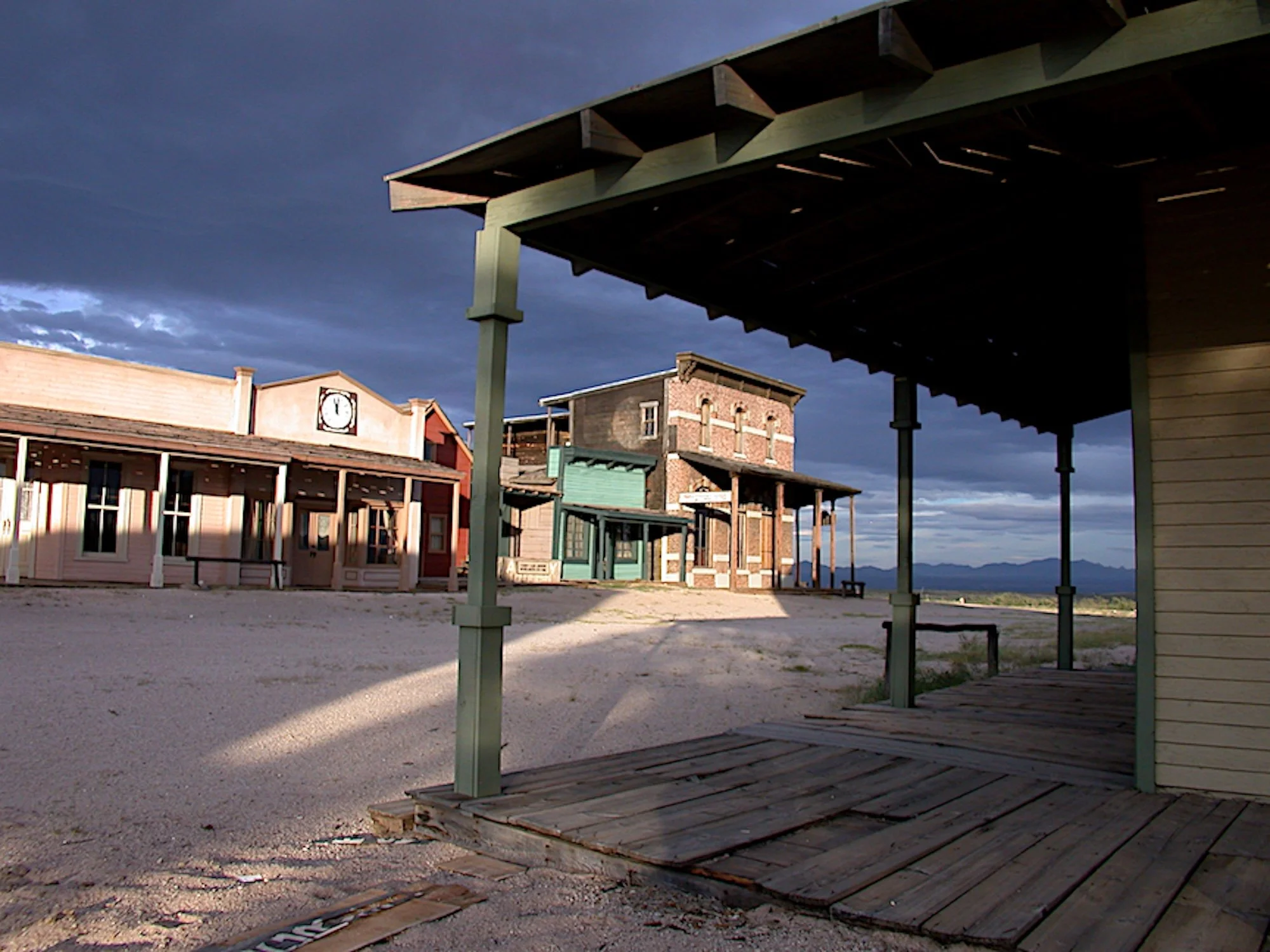 The film set town of Mescal, Arizona, at dusk, with old, wooden buildings and a clock tower, under a cloudy sky with the sun casting long shadows.