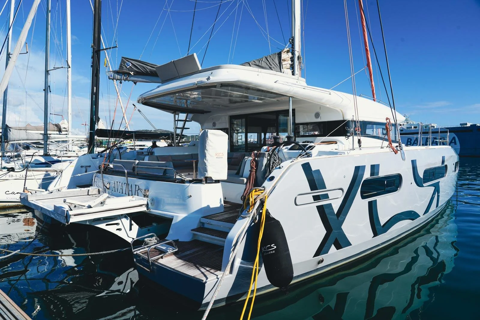 Luxury white yacht docked at marina with other sailboats, clear blue sky, and calm water.
