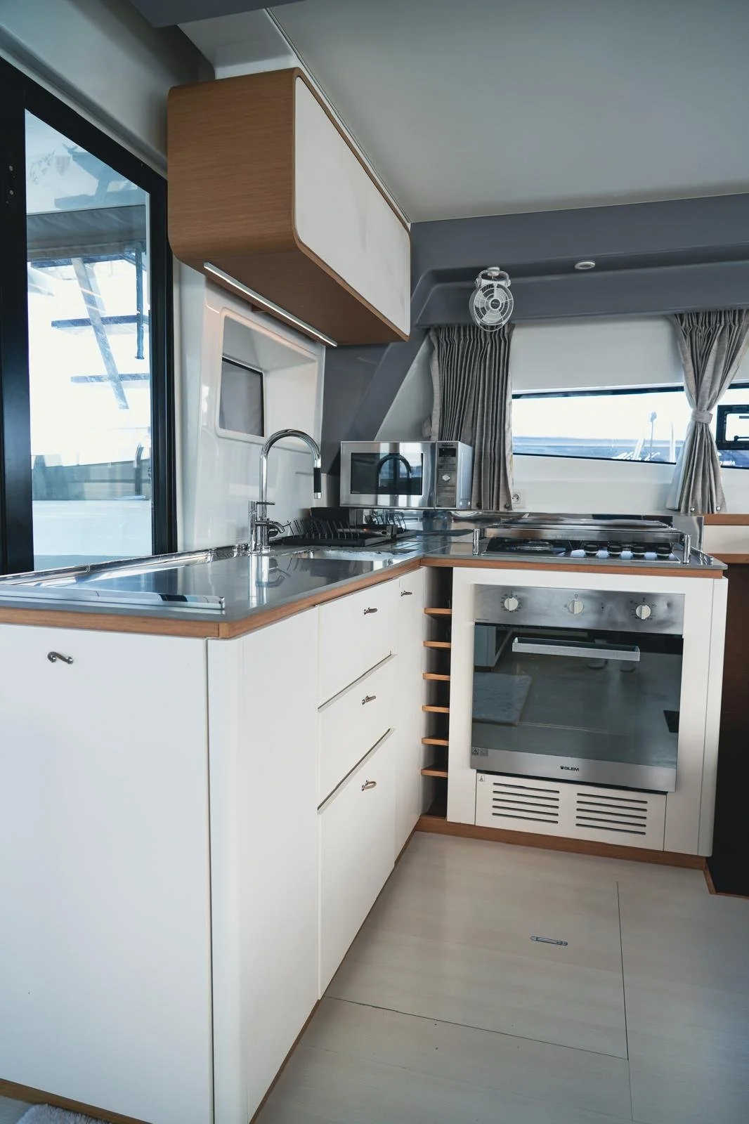 Modern boat kitchen with white cabinets, stainless steel sink, microwave, oven, and gas stove.