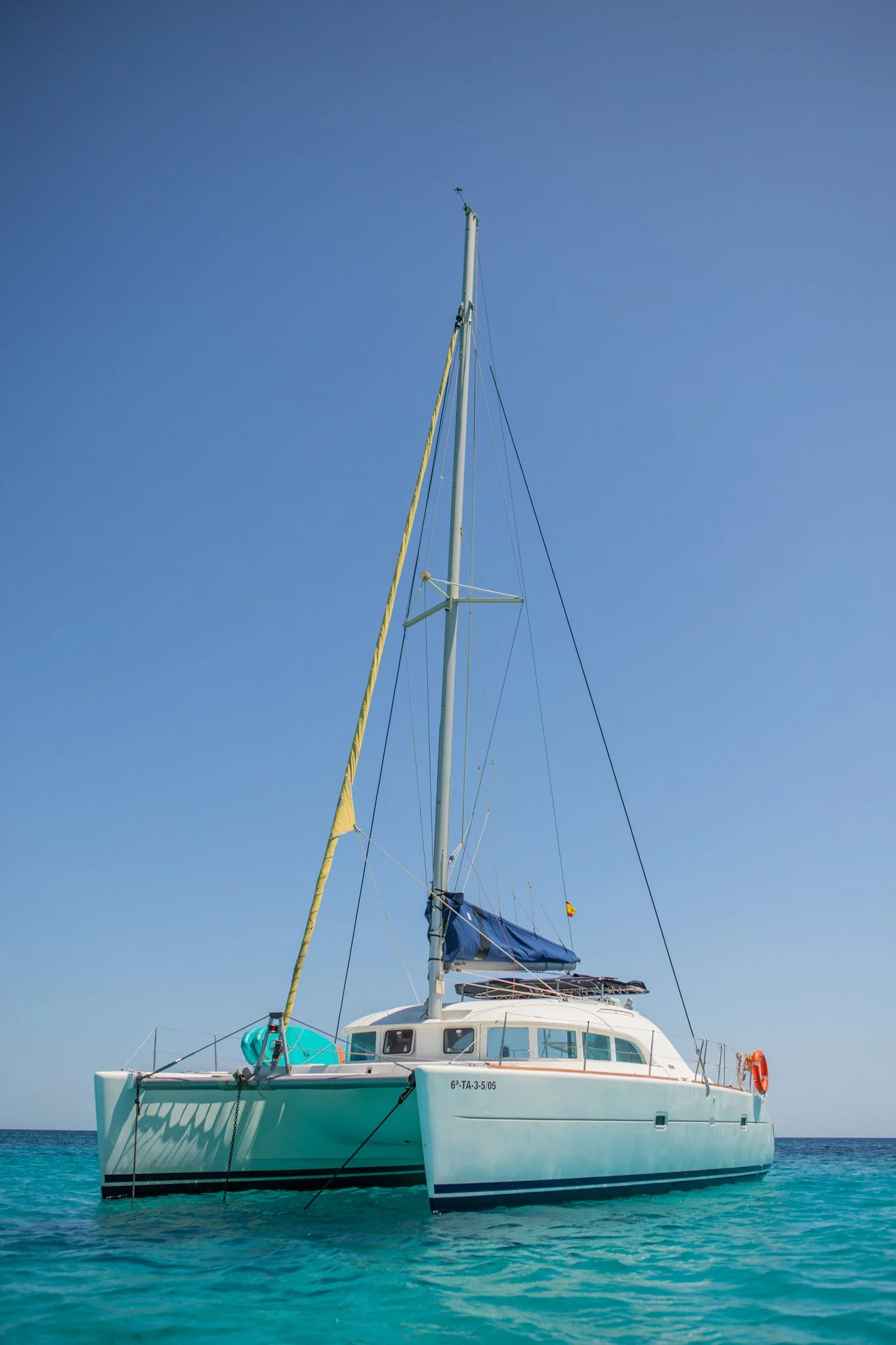A large sailboat with a white hull anchored in clear turquoise water under a blue sky.