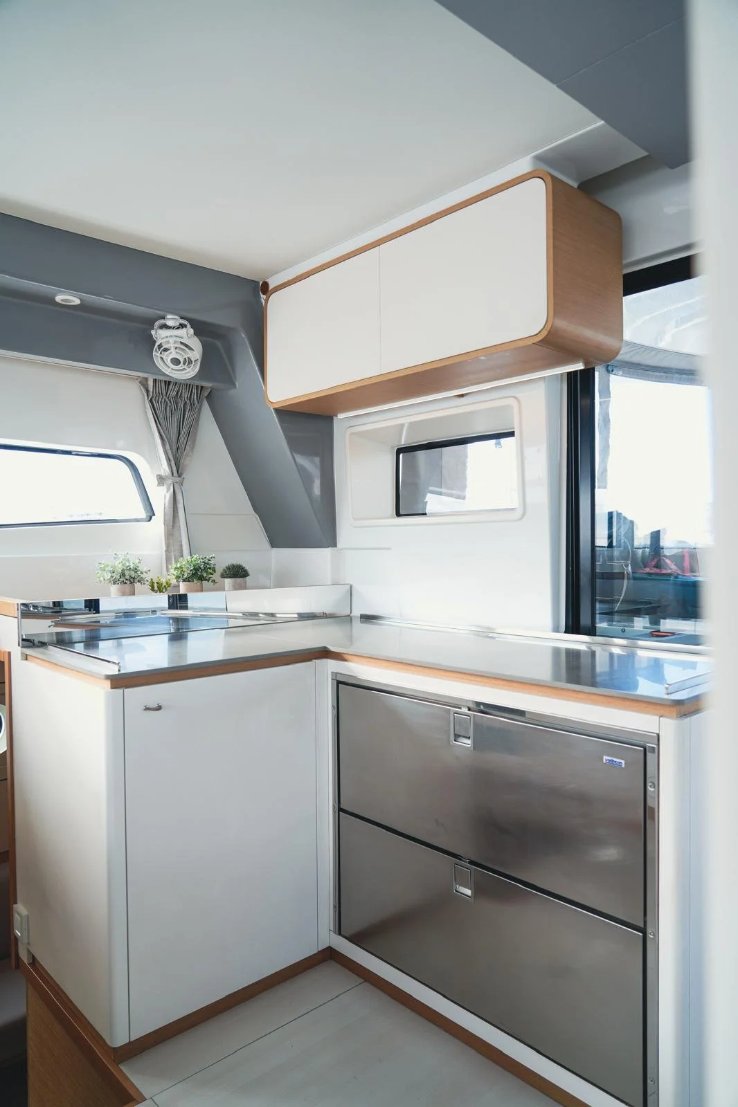 Modern compact kitchen with white cabinets, wooden trim, stainless steel appliances, a small window, and potted plants on the counter.