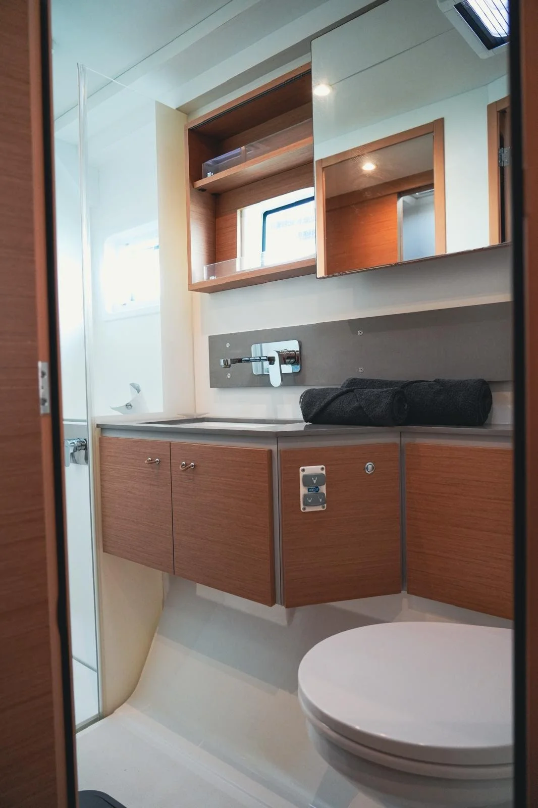 Small, modern bathroom with a wood vanity, mirror, window, and black rolled towel on the countertop, and toilet in the foreground.