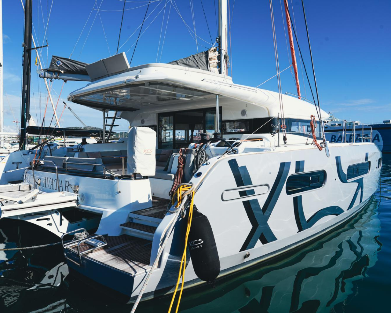 A white luxury yacht named Avazara docked at a marina under a clear blue sky, with other yachts visible in the background.