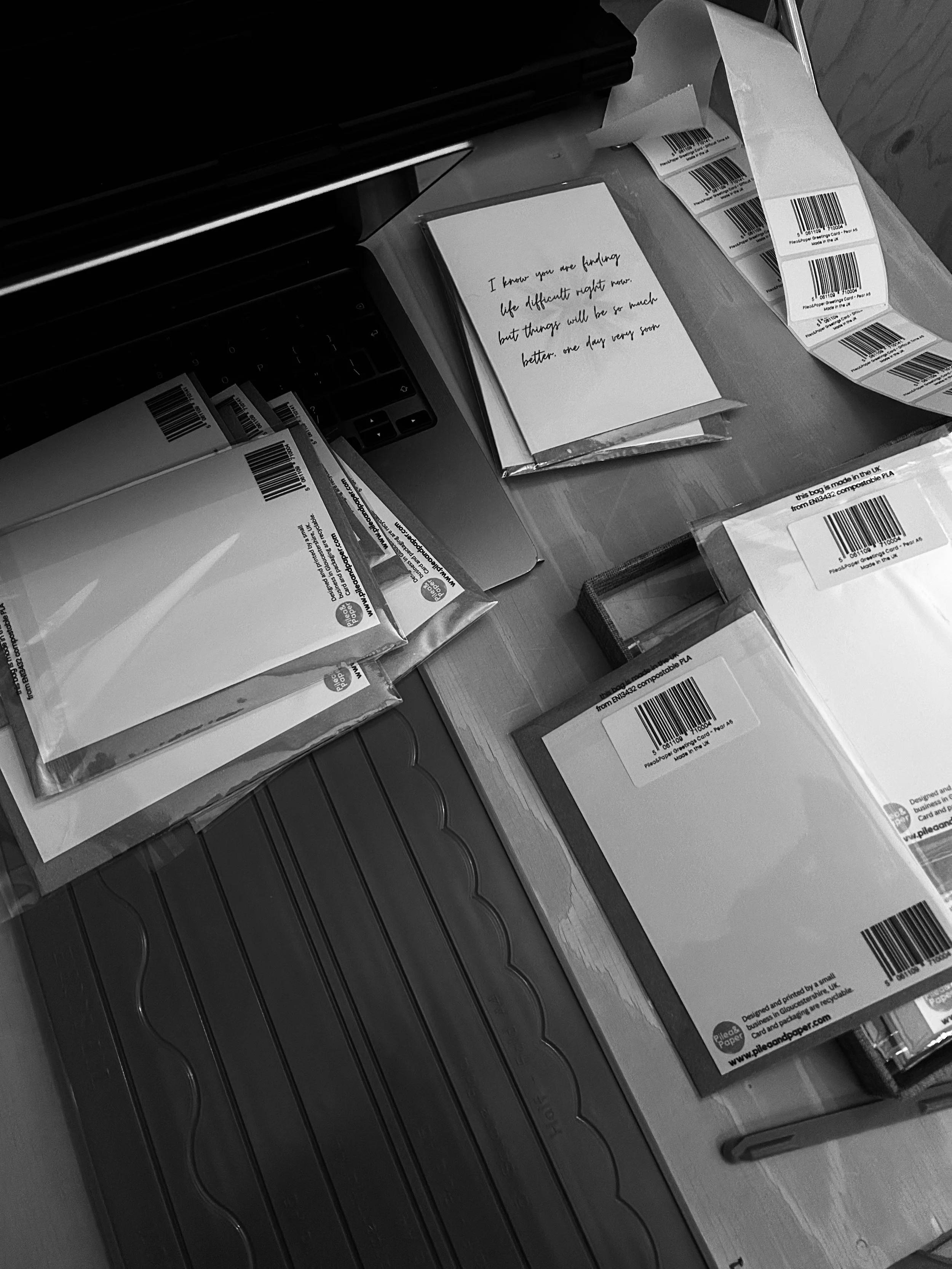 Several sheets of paper with barcodes and text, a handwritten note saying 'I know you are finding life difficult right now but things will be so much better one day very soon,' a black electronic device, and a small box on a wooden surface.