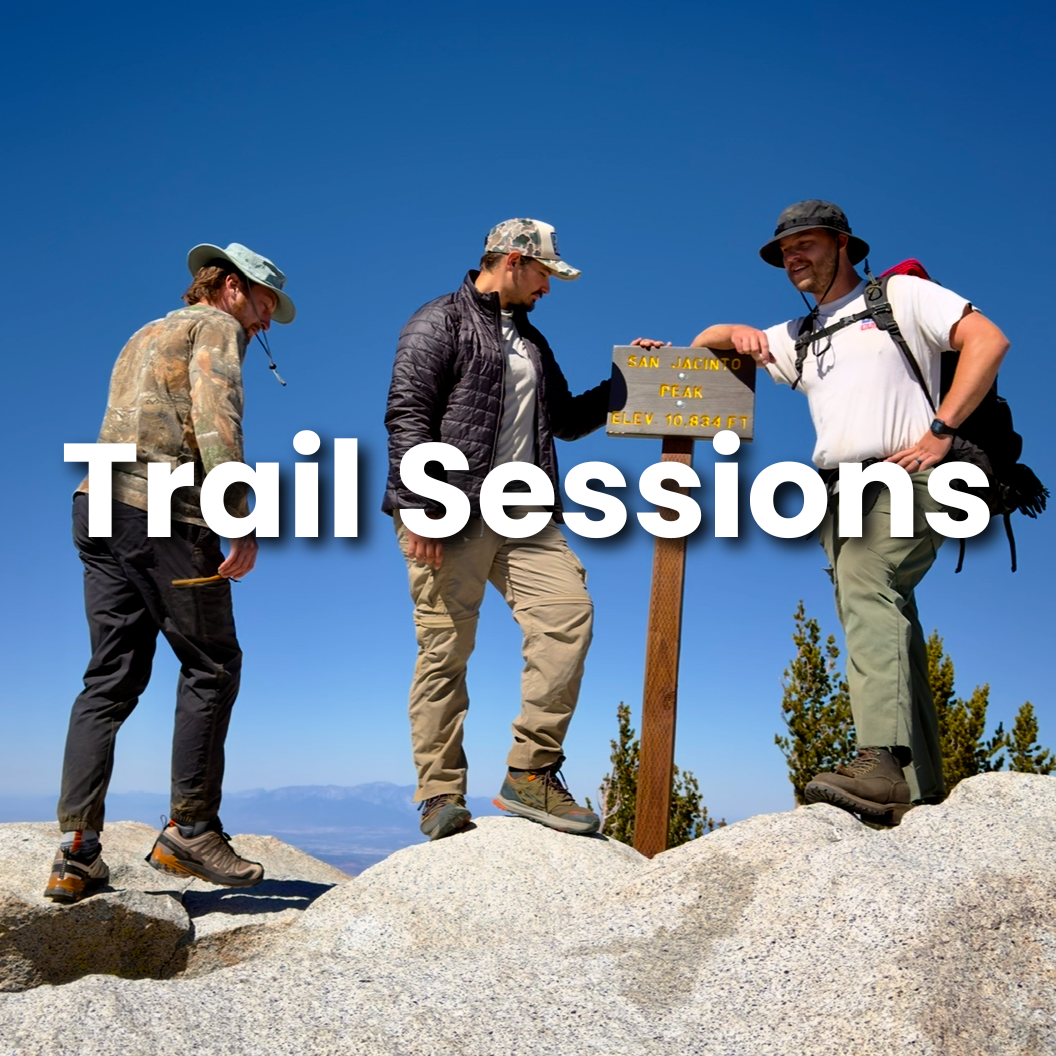 Three hikers standing on a mountain summit, with one holding a sign that reads "San Jacinto Peak Elev. 10,834 ft," under a clear blue sky. The words "Trail Sessions" are overlaid on the image.