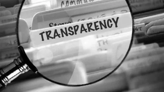 A magnifying glass focusing on a sign that reads 'TRANSPARENCY' on a bookshelf or display.