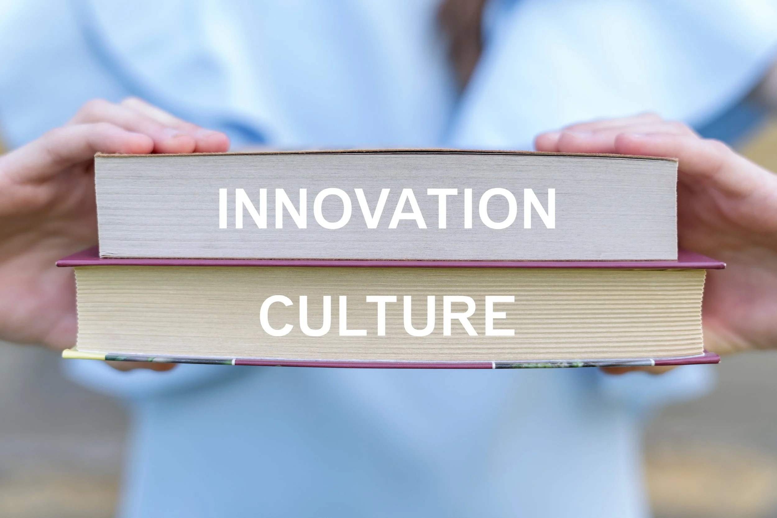 Person holding a stack of books with the titles 'INNOVATION' and 'CULTURE' visible on the spines.