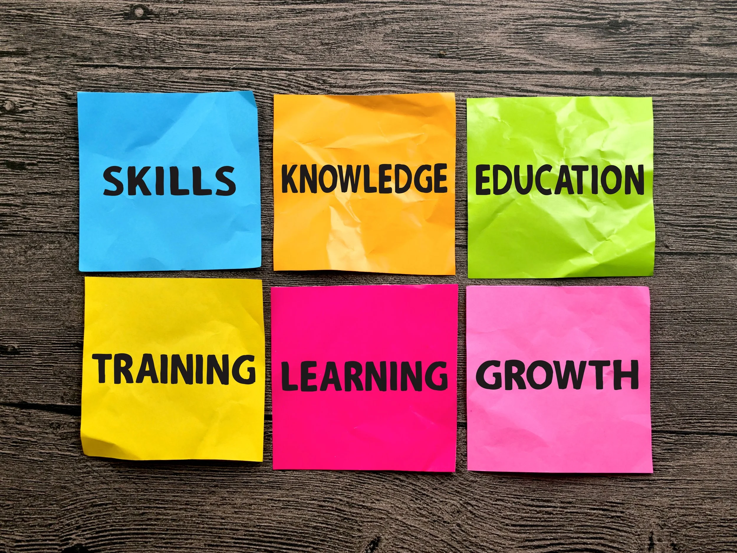 Colorful sticky notes on a wooden surface with words Skills, Knowledge, Education, Training, Learning, Growth.