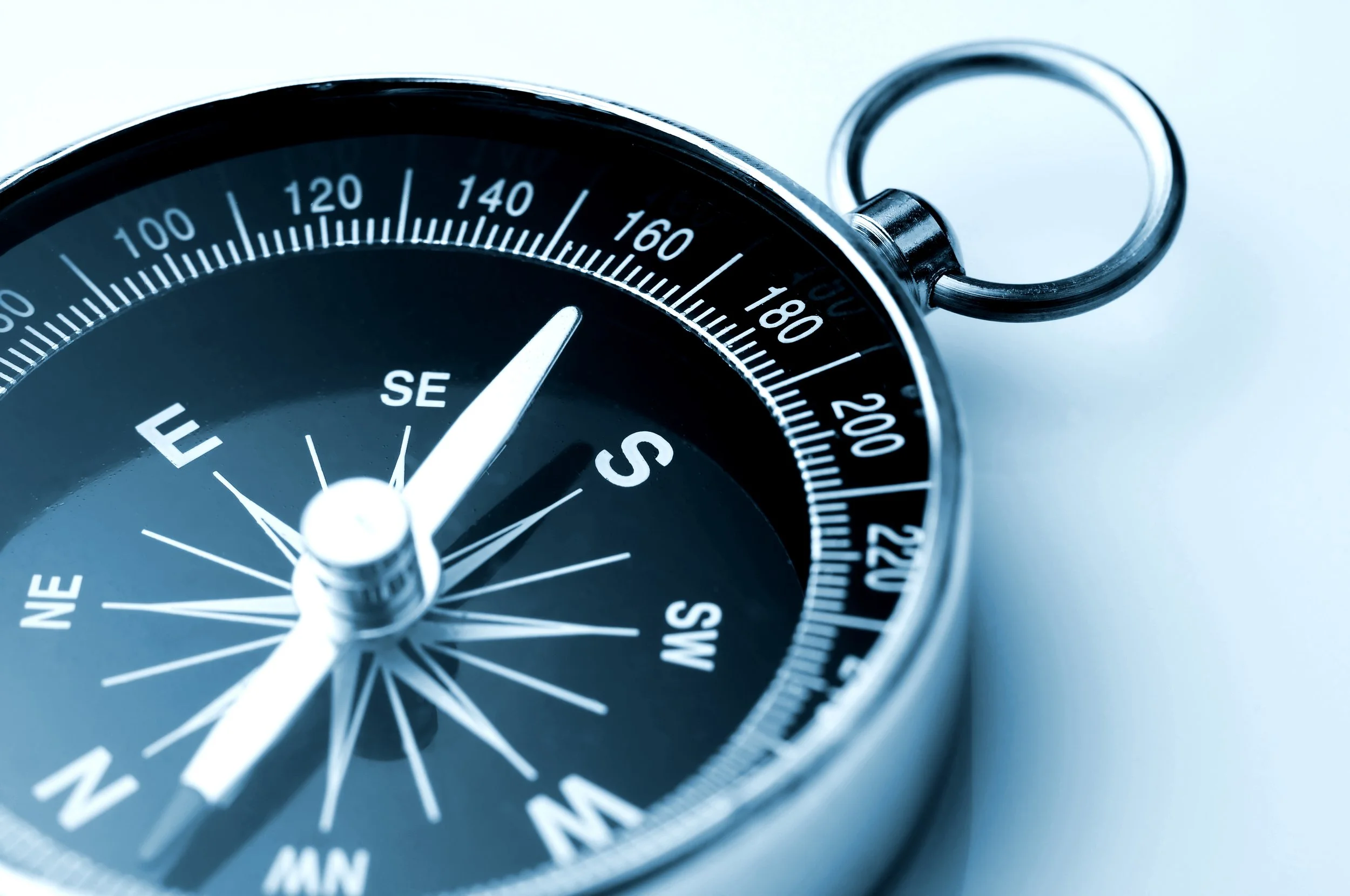 Close-up of a compass showing directions and degree markings, with a metallic ring attached.