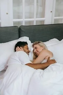 A couple lying in bed, smiling and looking at each other, with the woman hugging the man.
