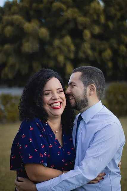 A couple smiling and embracing outdoors in front of trees.