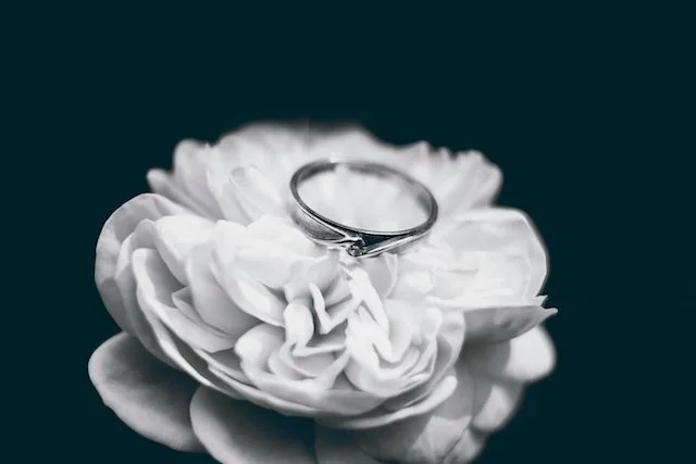 A silver ring resting on a white flower against a dark background.