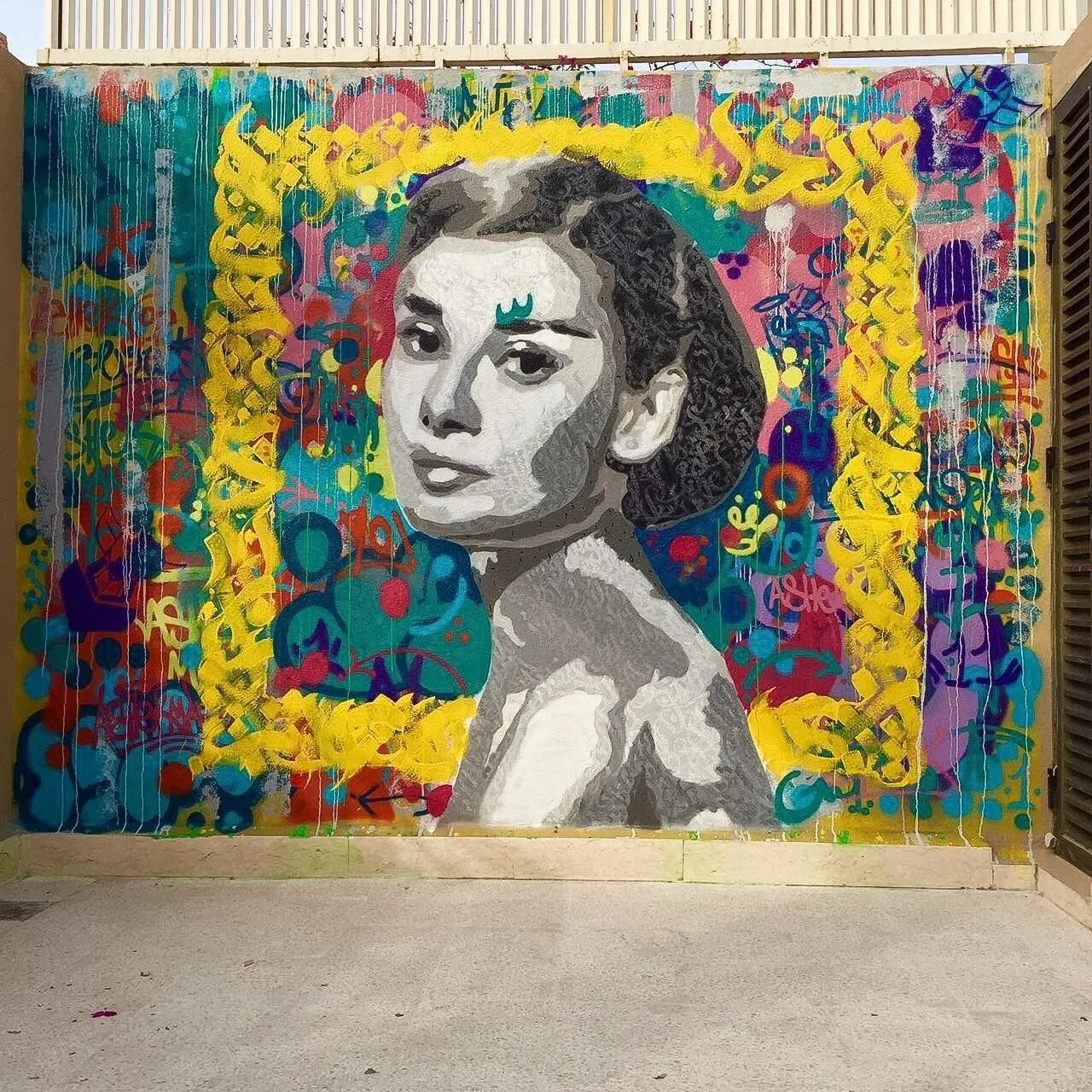 Street art mural of a woman’s portrait with a colorful abstract background and yellow decorative border.