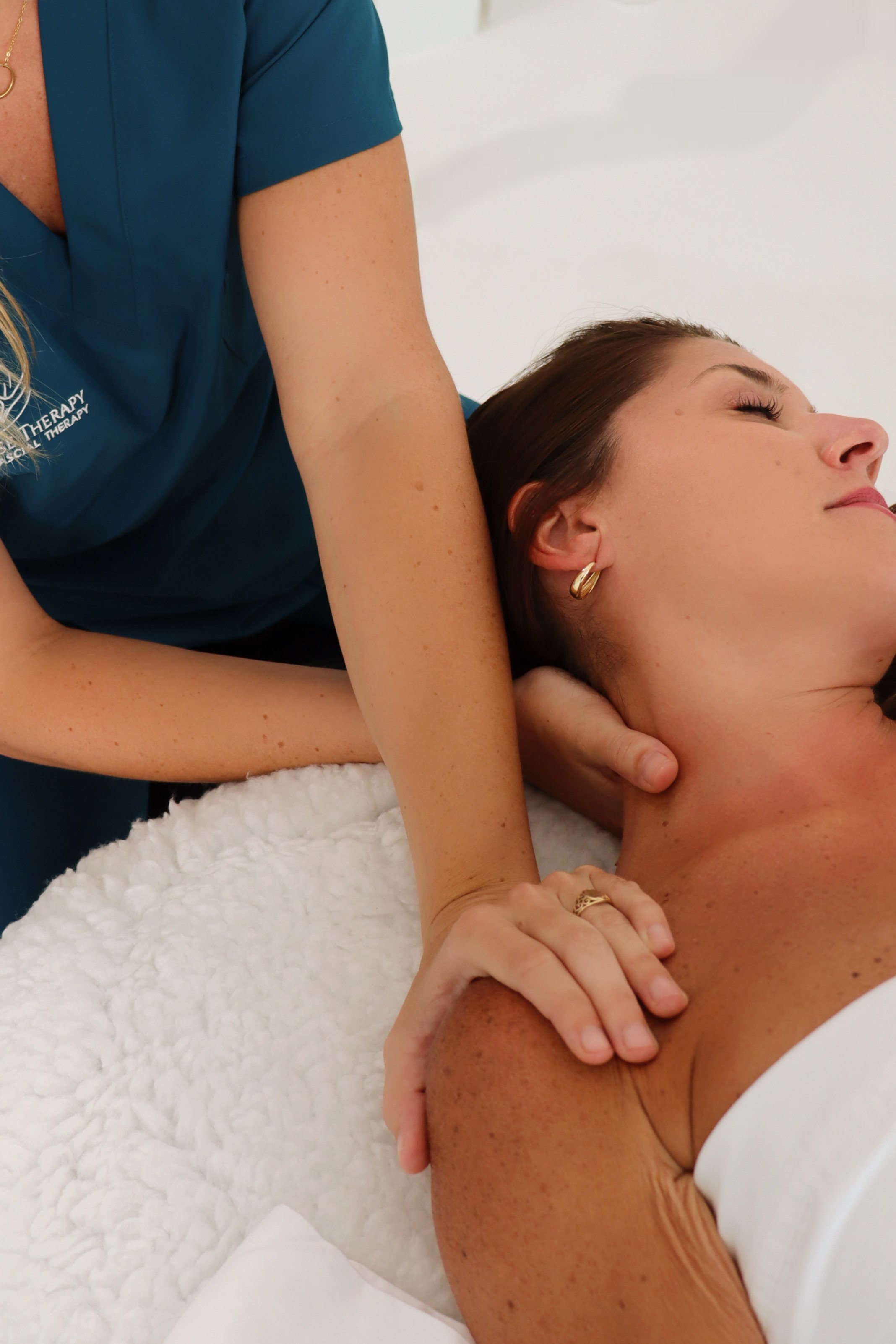 Person lying on a massage table receiving a shoulder and neck massage from a therapist.