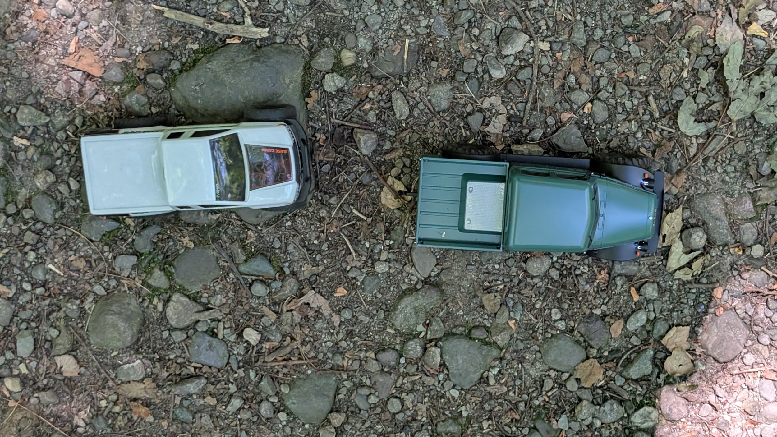 An overhead view of two RC vehicles, driving on rocky ground outdoors.