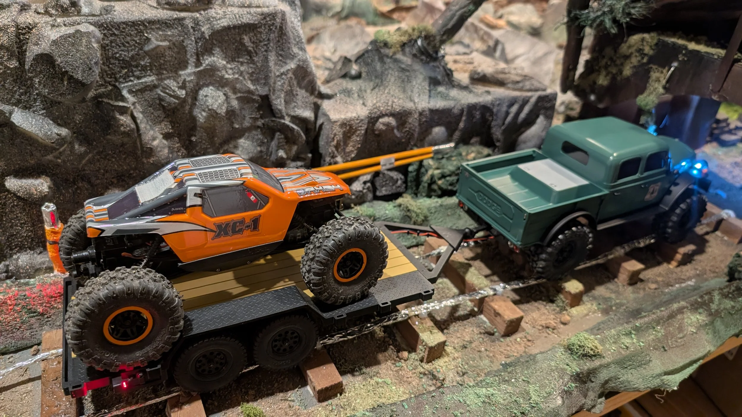 Remote-controlled toy off-road trucks on a miniature rugged terrain with rocks and elevation, simulating a mountain rail trail