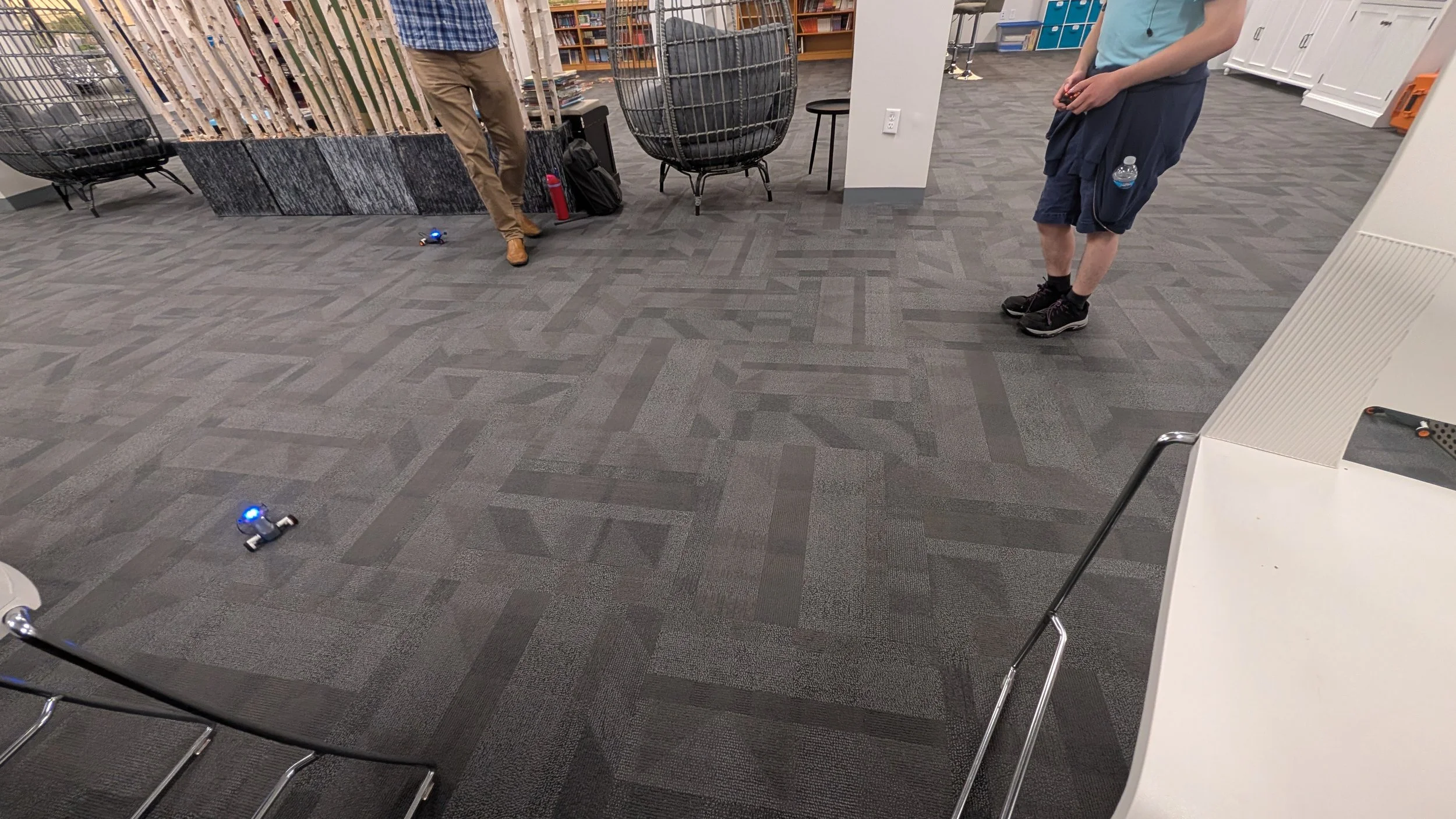 Two robots from a STEM workshop being tested on the floor, two people standing nearby.