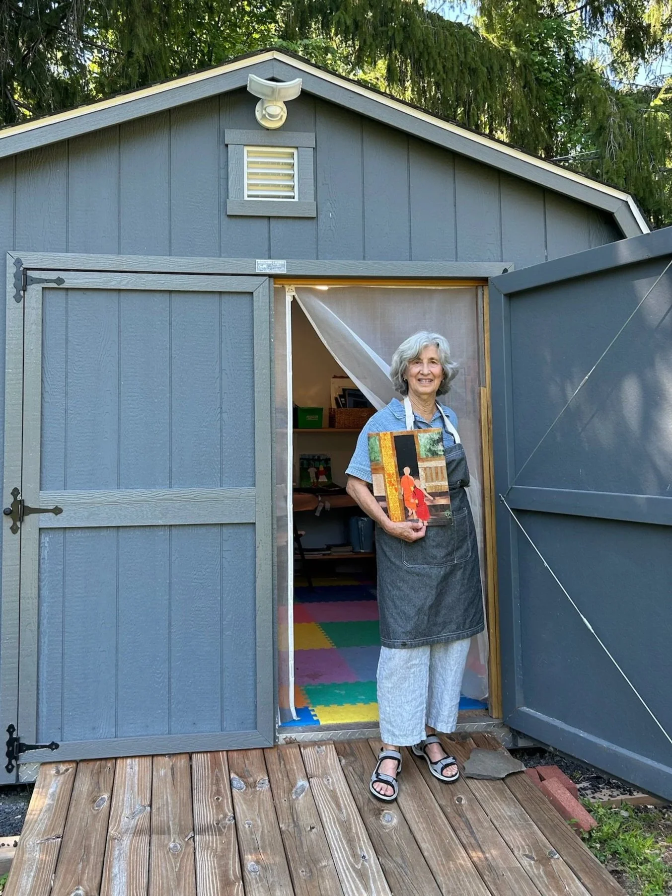 Alice goodman standing in front of her art studio in Woodstock, NY holding a piece of her art on a sunny day