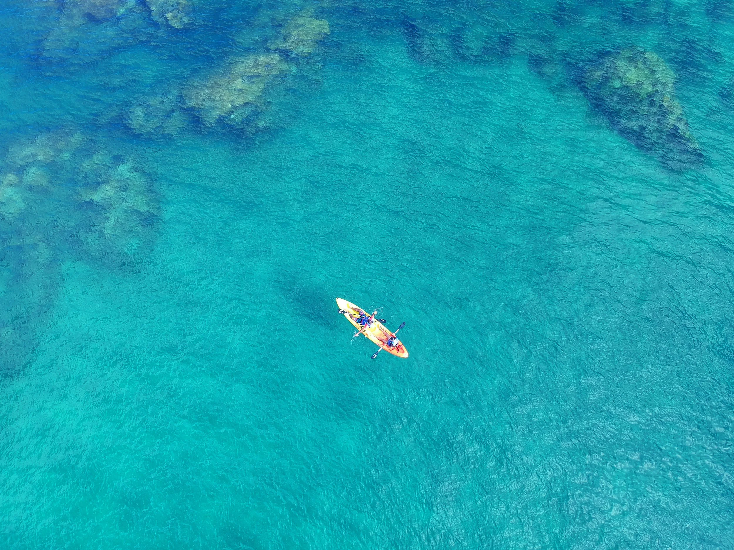 An aerial view of a kayak on clear blue water, with a person sitting in it.