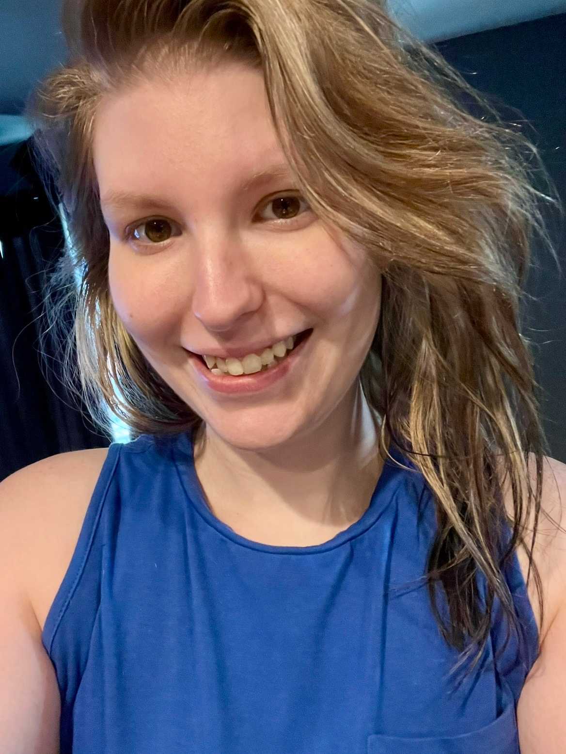 A young woman with wavy, shoulder-length hair, wearing a sleeveless blue top, smiling at the camera.