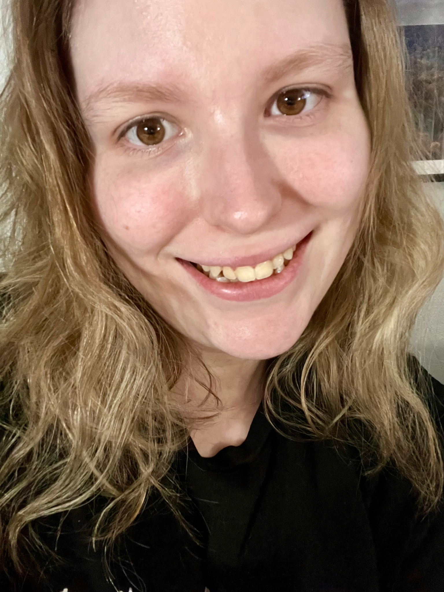 Close-up of a smiling woman with long, curly blonde hair and brown eyes, wearing a black top.