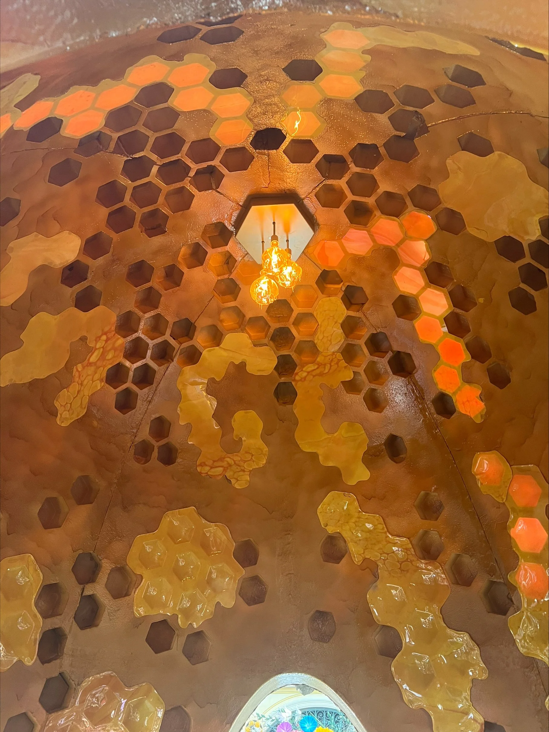 Close-up of a cone's interior with honeycomb-shaped holes and decorative amber-colored elements, lit by a hanging warm-toned light fixture.