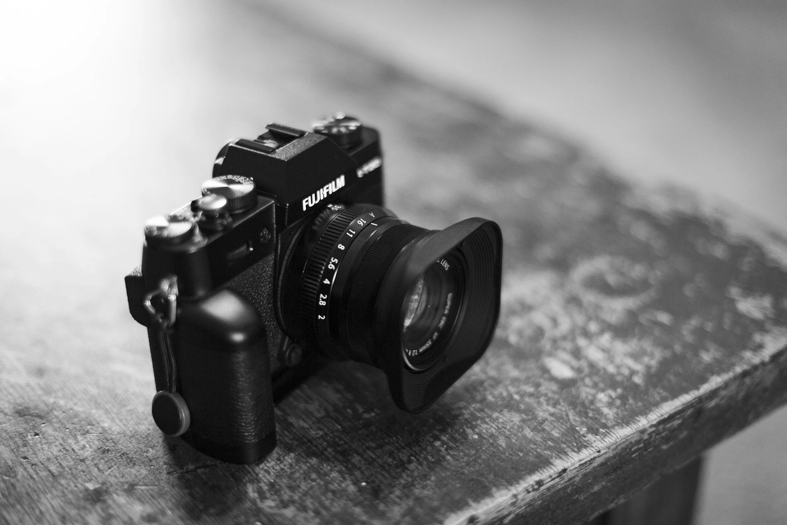 Black Fujifilm camera with a lens, placed on a wooden surface.