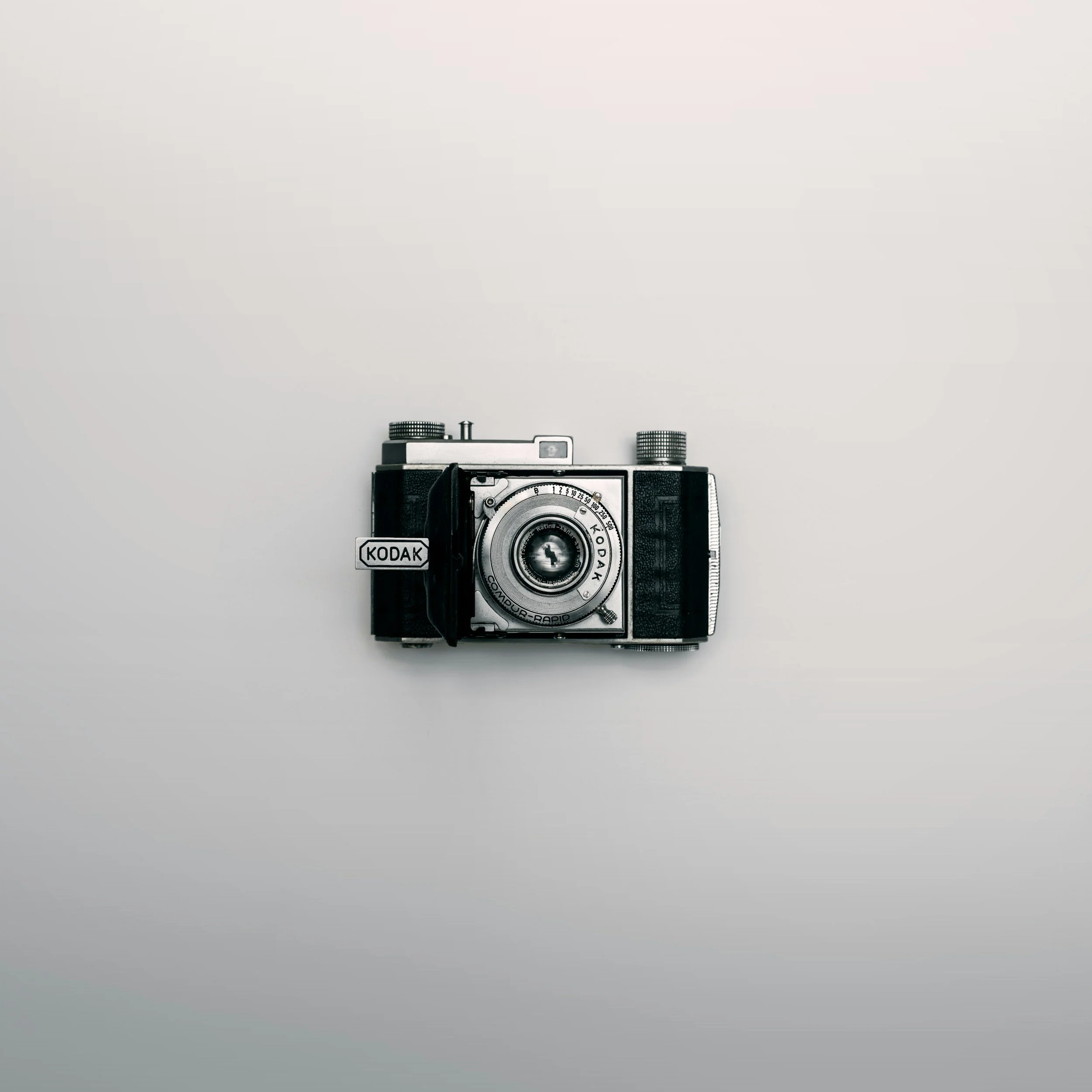 A vintage Kodak camera with a silver and black body, placed on a light gray background.