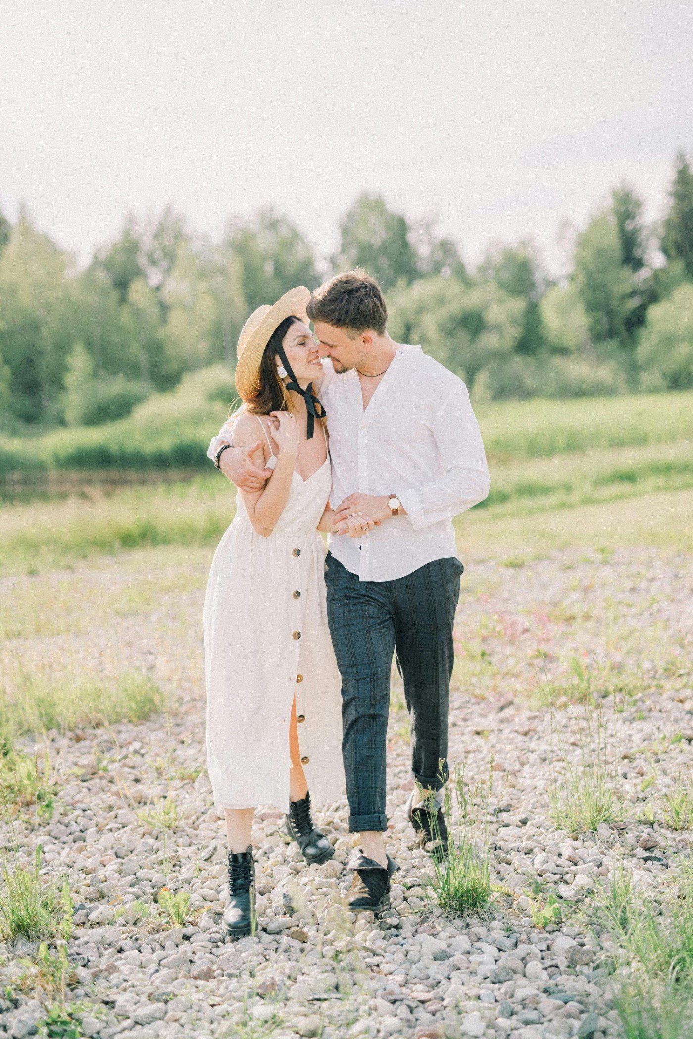 A young couple walking on a rocky path outdoors, smiling and embracing, with greenery in the background.