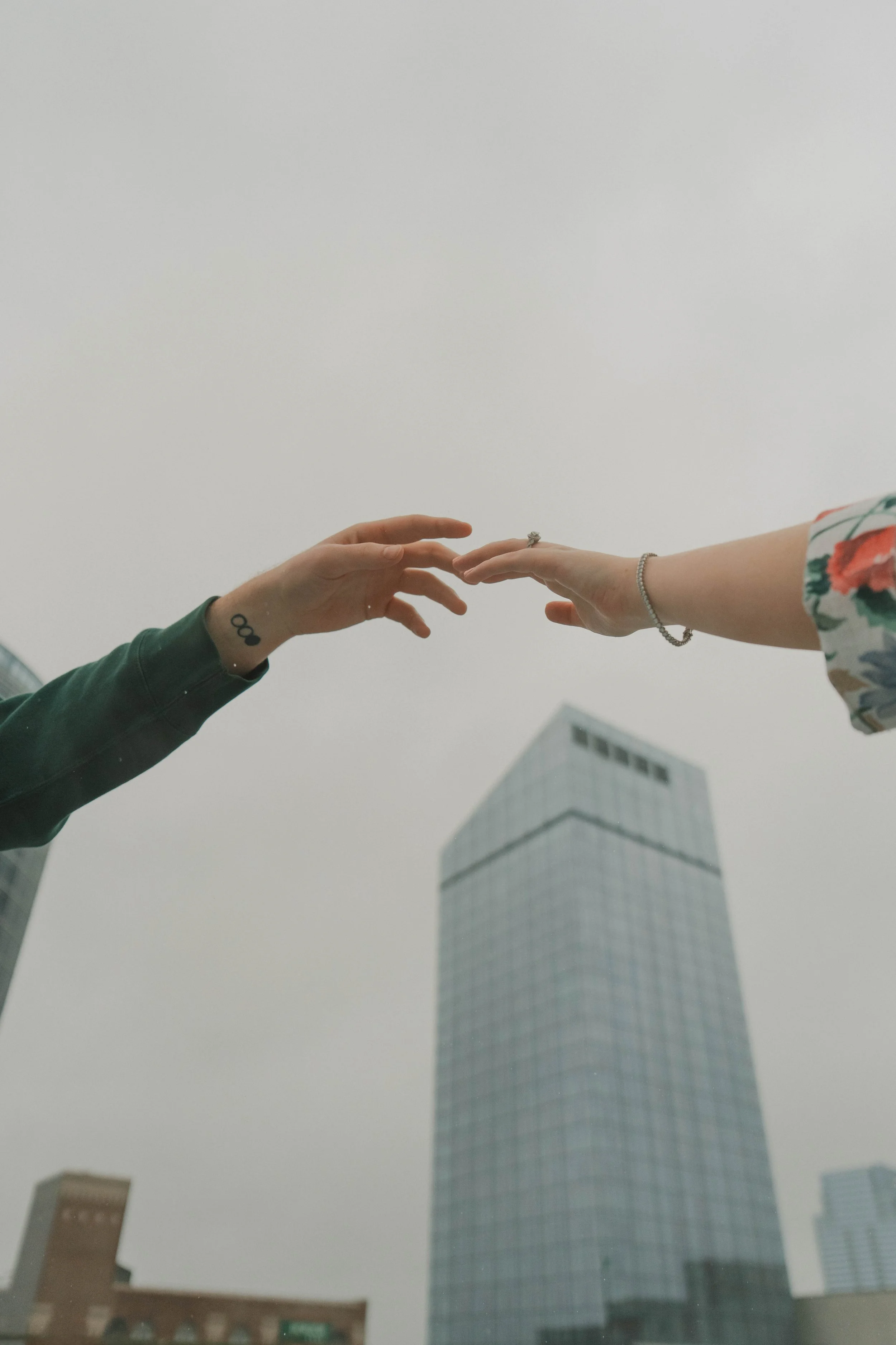 Two hands reaching towards each other with a city building in the background.