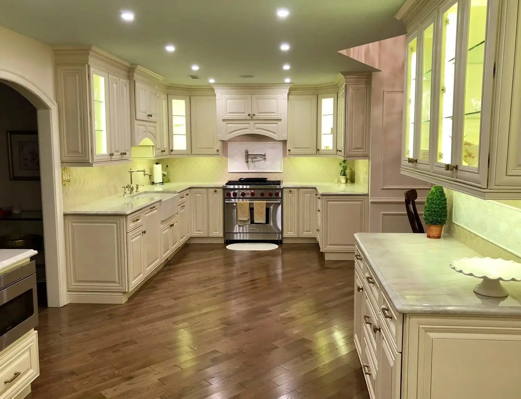 Bright kitchen with white cabinetry, a stainless steel stove, yellow backsplash, and hardwood floors. Multiple ceiling lights, a small potted plant, and decorative items on the counters.