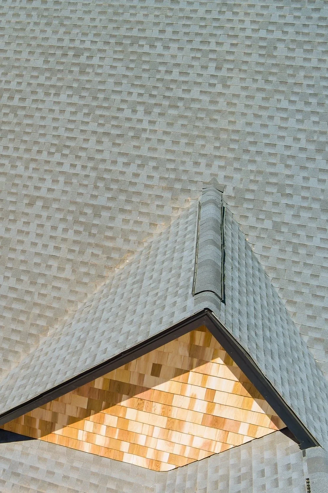 Aerial view of a house with a light gray shingled roof and a gable with wooden shingles.