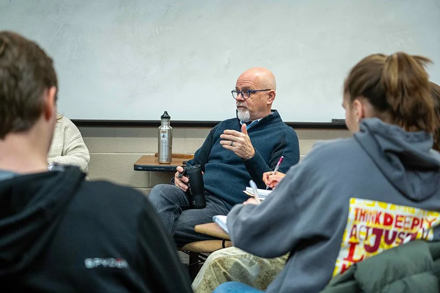 Tom Medema sits in a classroom and talks with students at Calvin university about his career