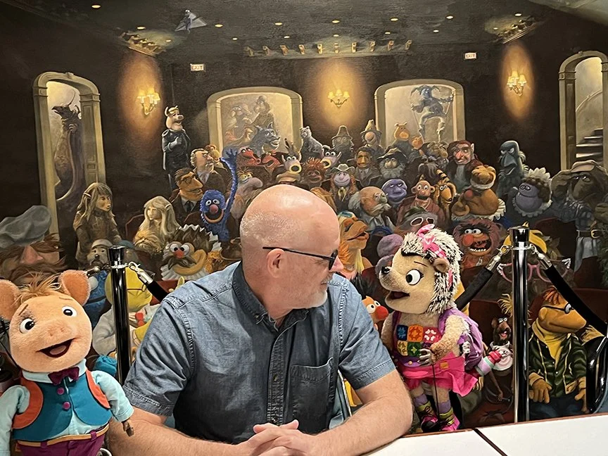 Tom Medema talks with Jim Henson puppets Roxy and Ronald at a table in Jim Henson board room