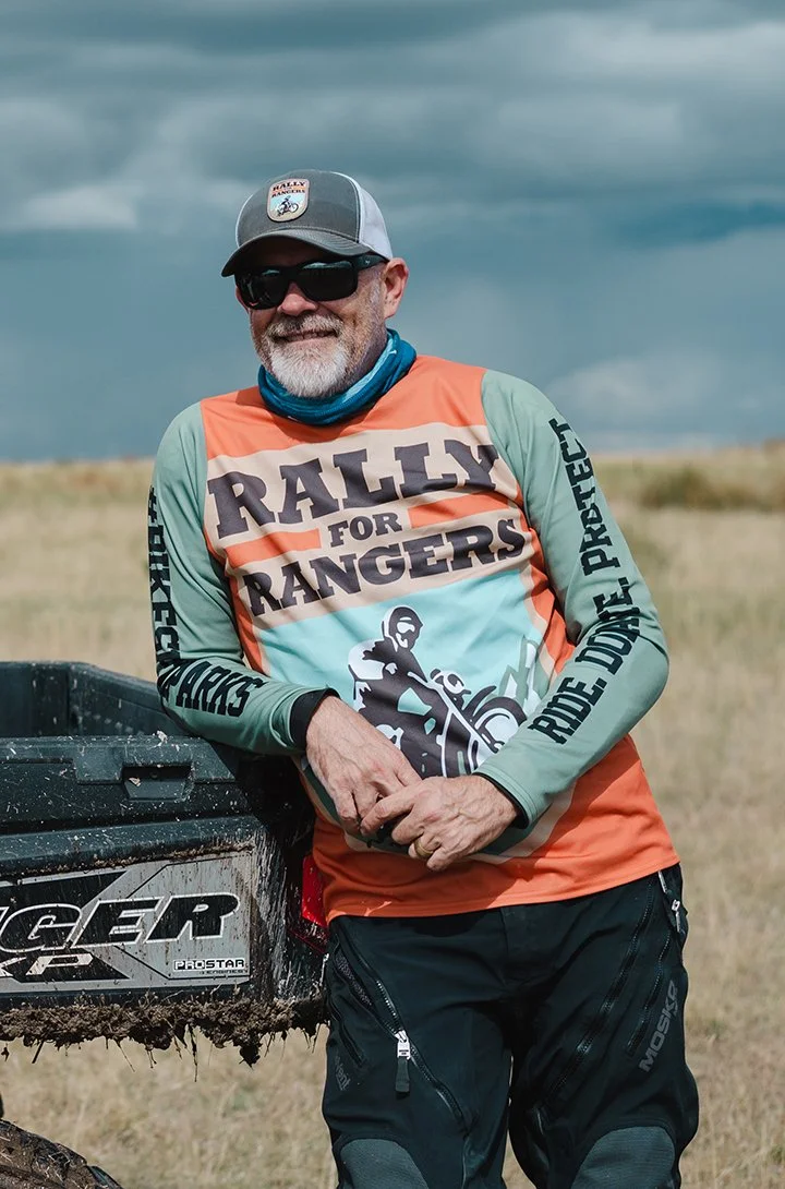 Tom Medema wearing Rally for Rangers motorcycle jersey and ball cap leans on a side-by-side bed in a meadow