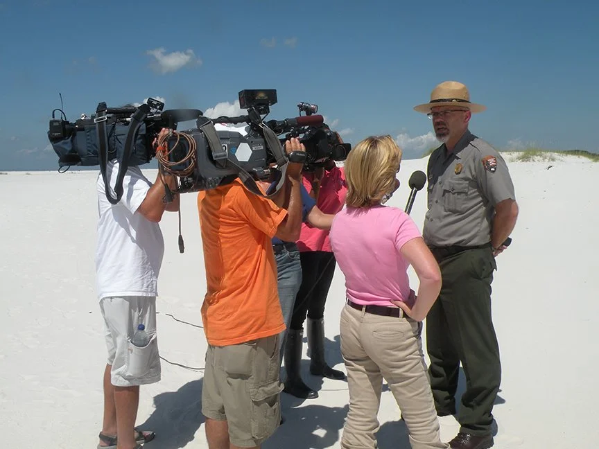 Tom Medema speaks to a half dozen reporters and camera operators on a beach during the Deepwater Horizon Oilspill
