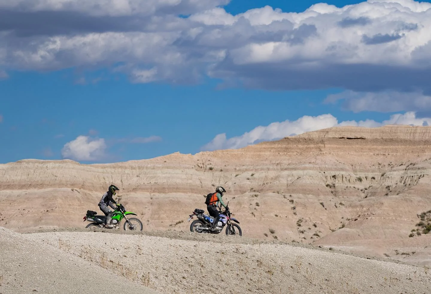two dual sport motorcycles ride a gravel road with the South Dakota badlands in the background