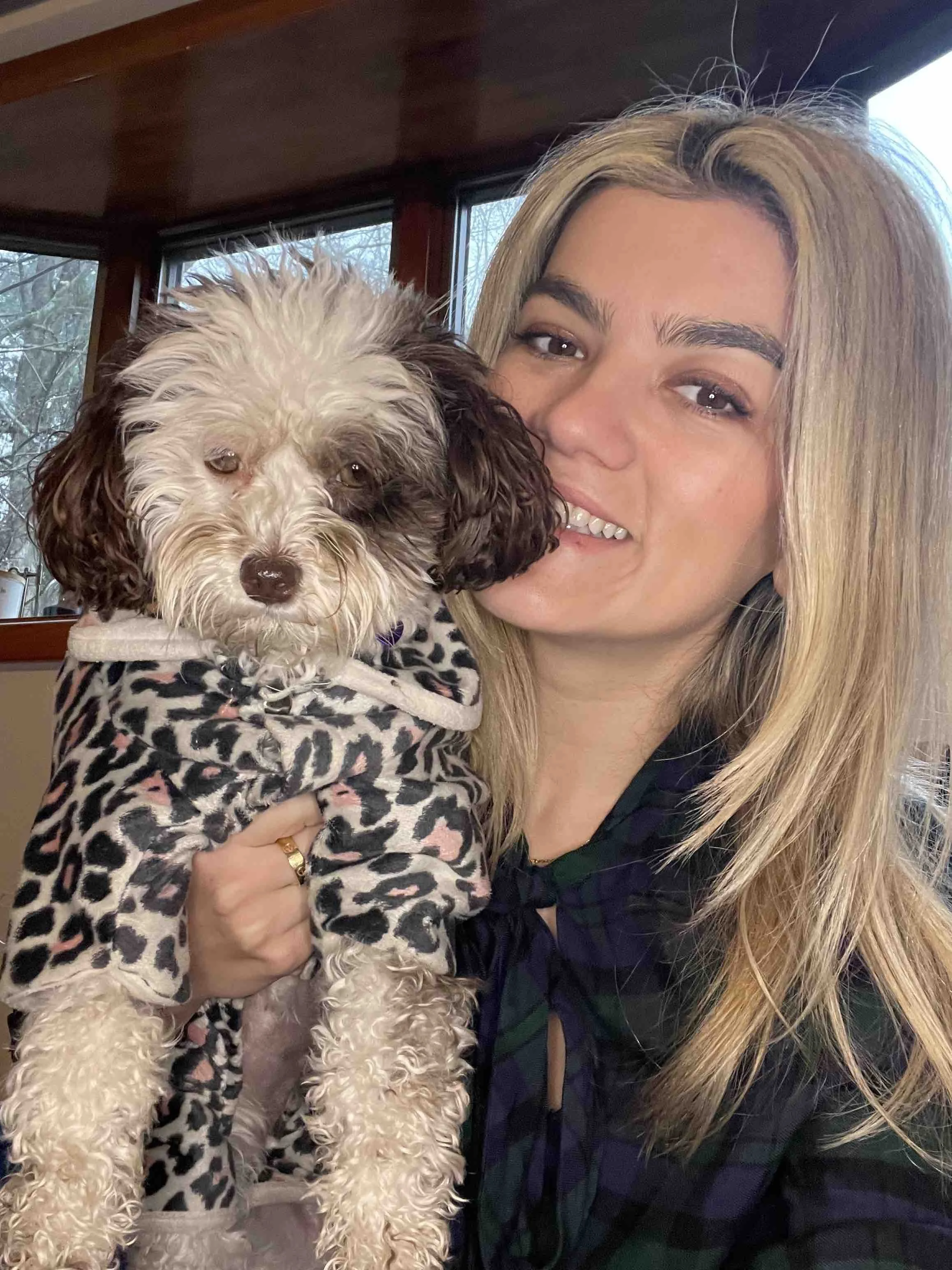 Smiling woman holding a dog that is wearing a leopard print shirt