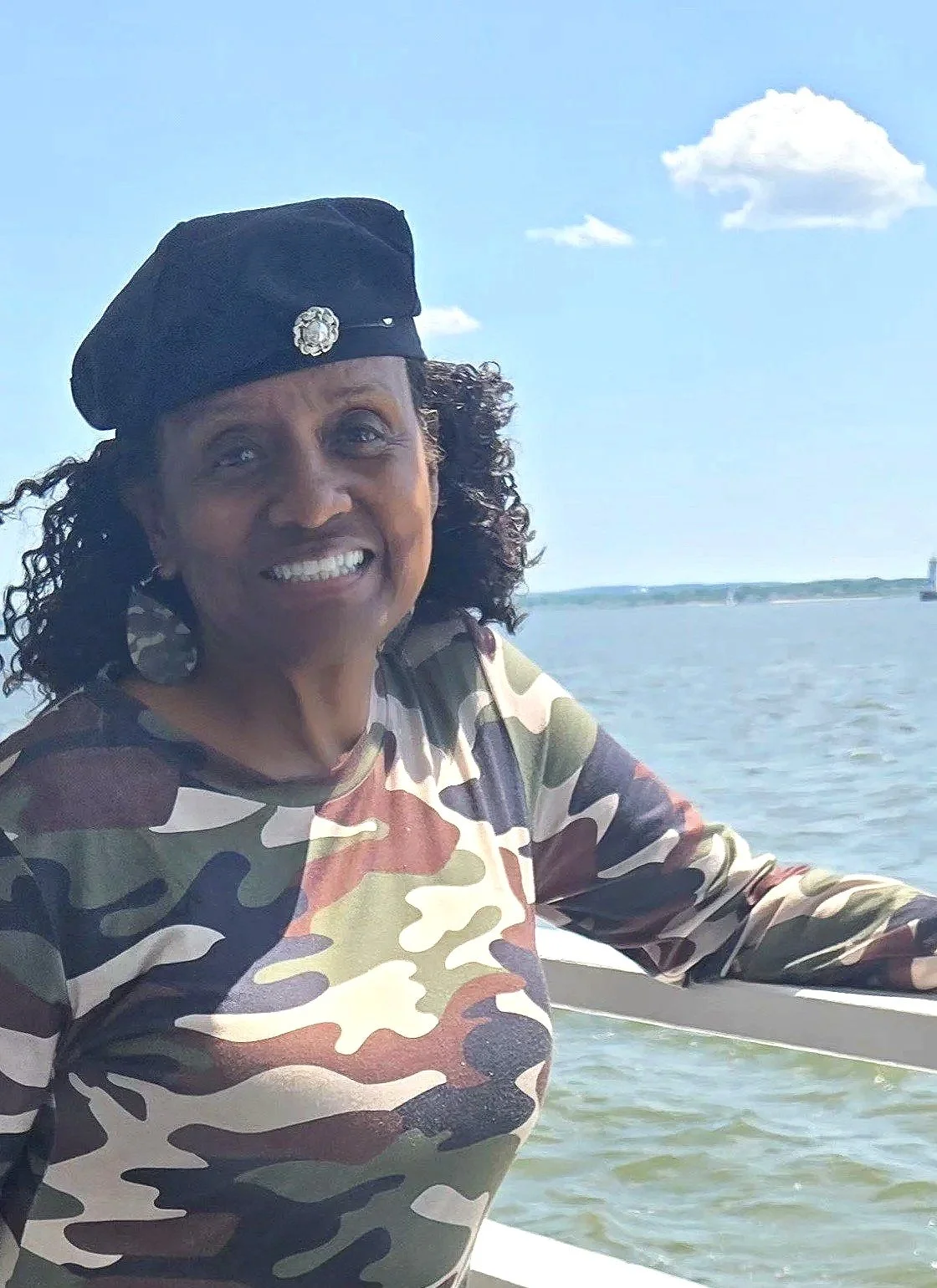Photo of a smiling woman standing next to the ocean wearing a black beret