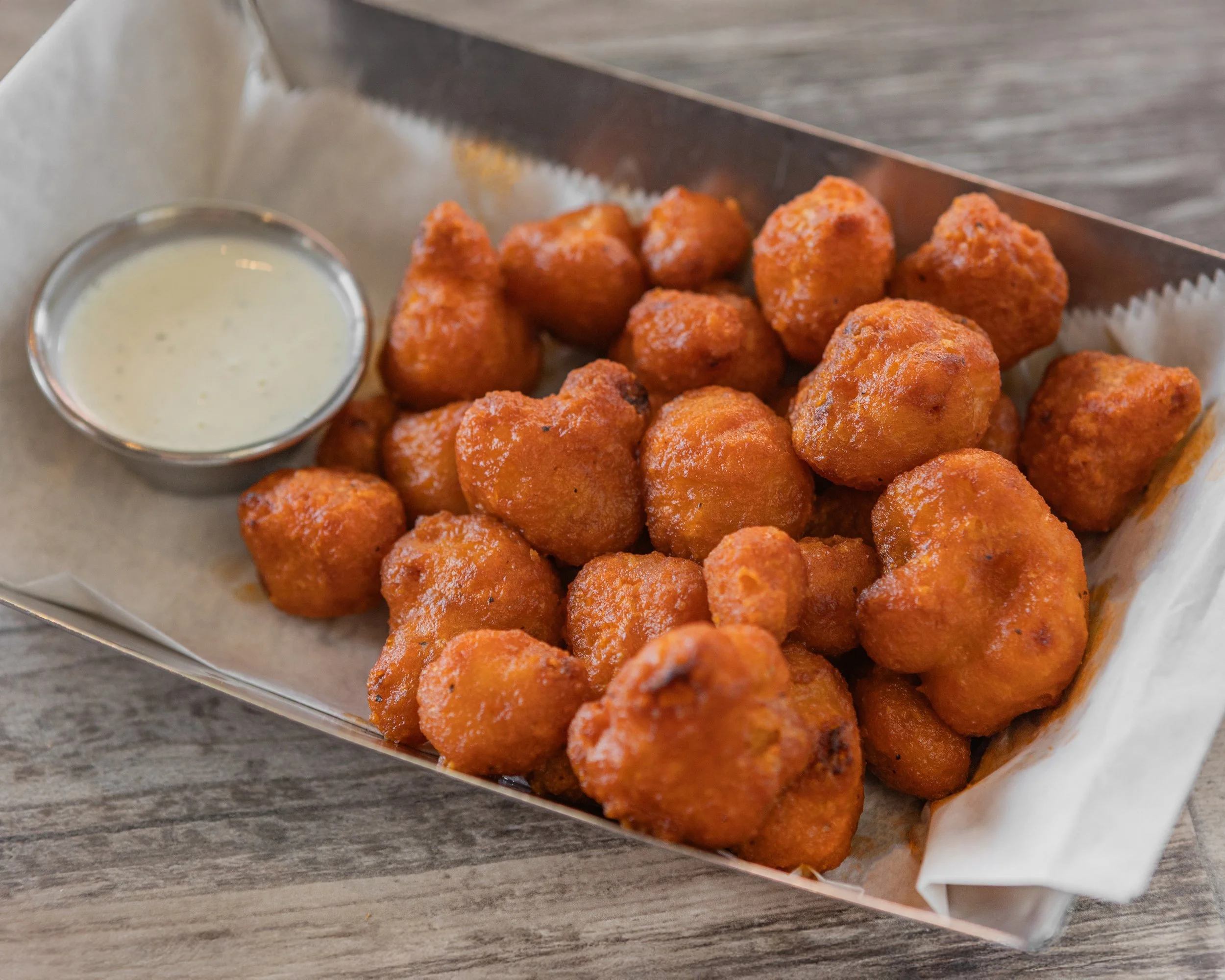 A tray of fried buffalo chicken balls with a small cup of dipping sauce on a wooden table.