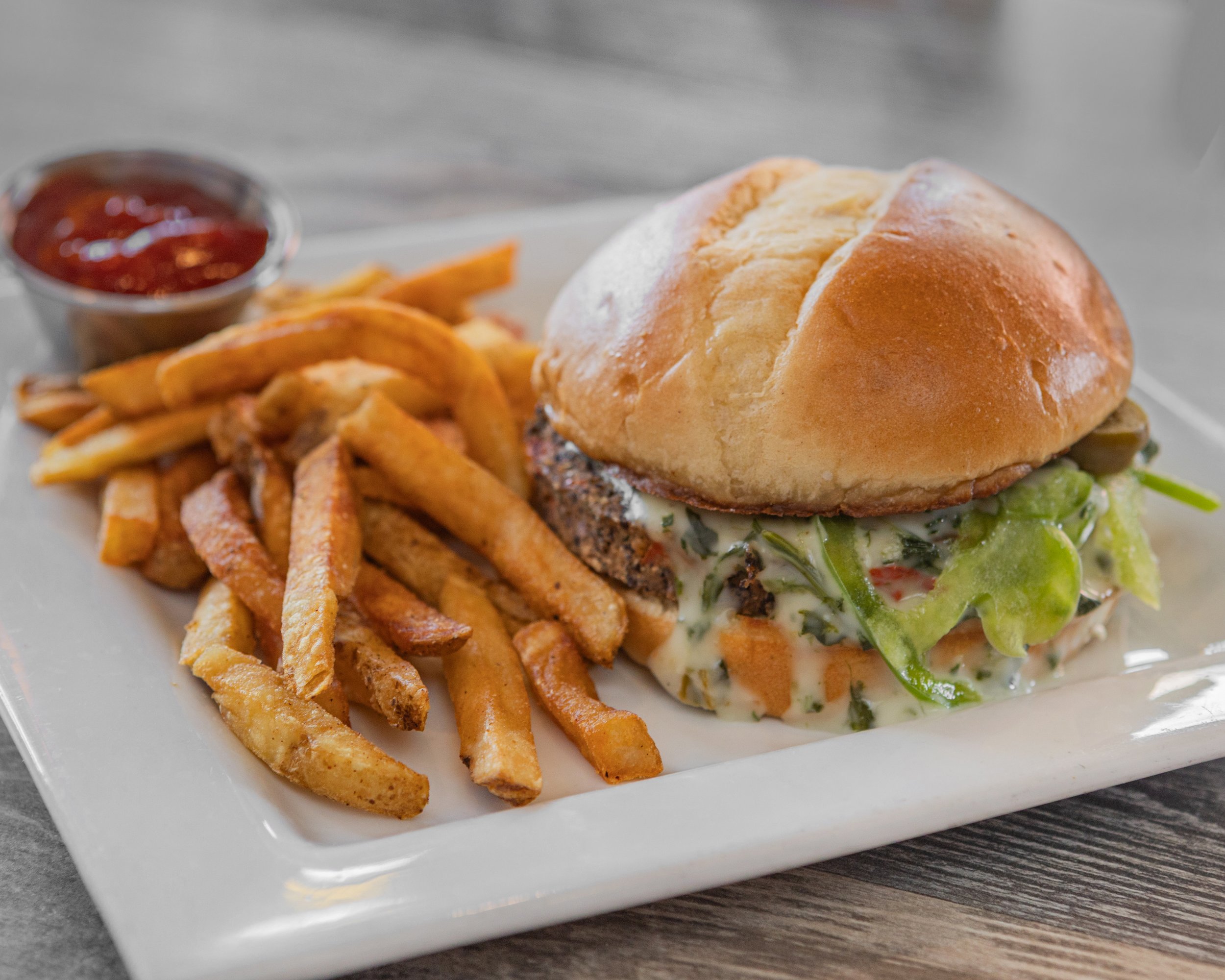 A sandwich with a bun, lettuce, and meat, served with French fries and a side of ketchup.
