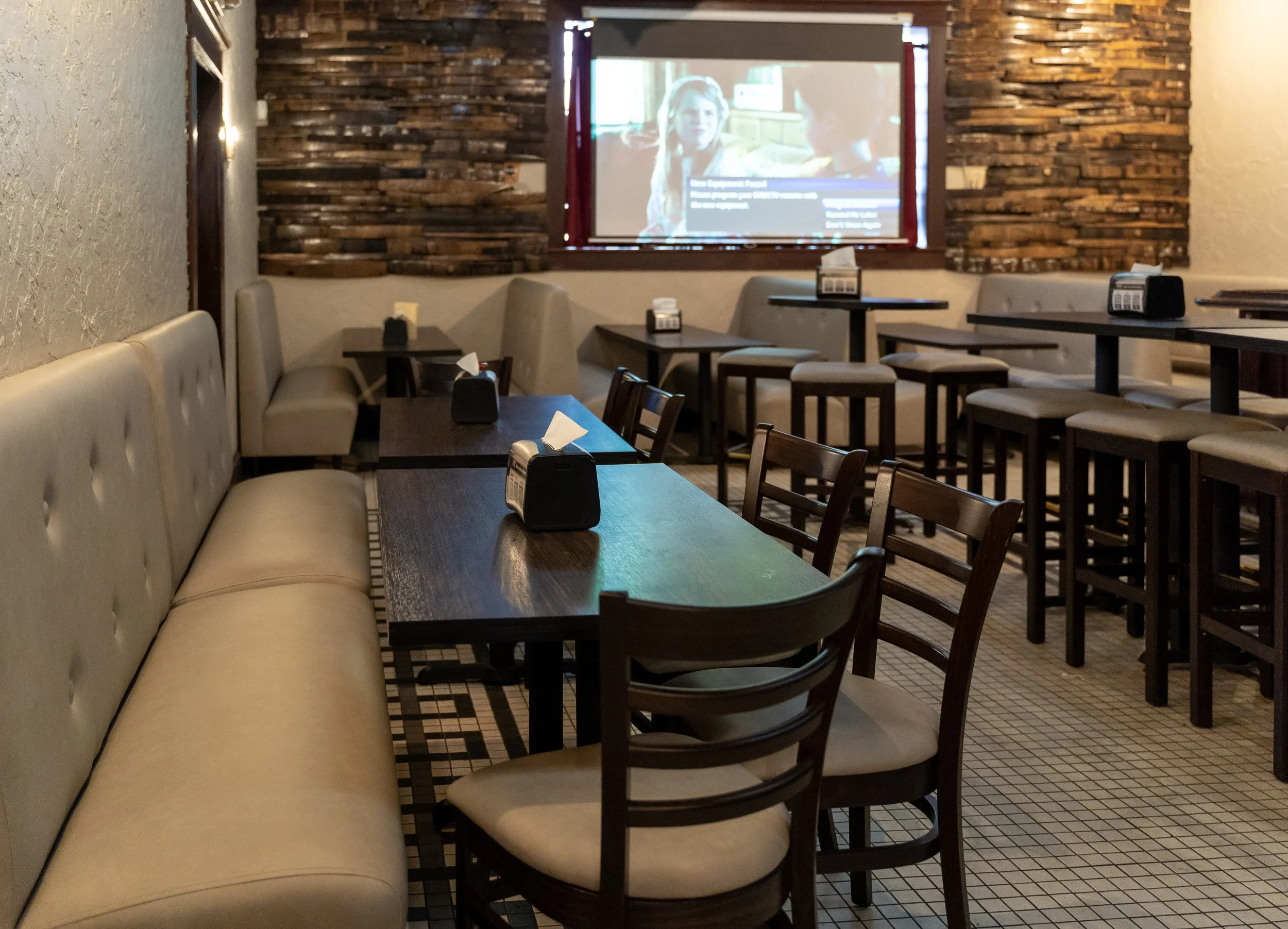 Empty restaurant with tables, chairs, tissue boxes, and a large screen TV showing a movie with two women in conversation.