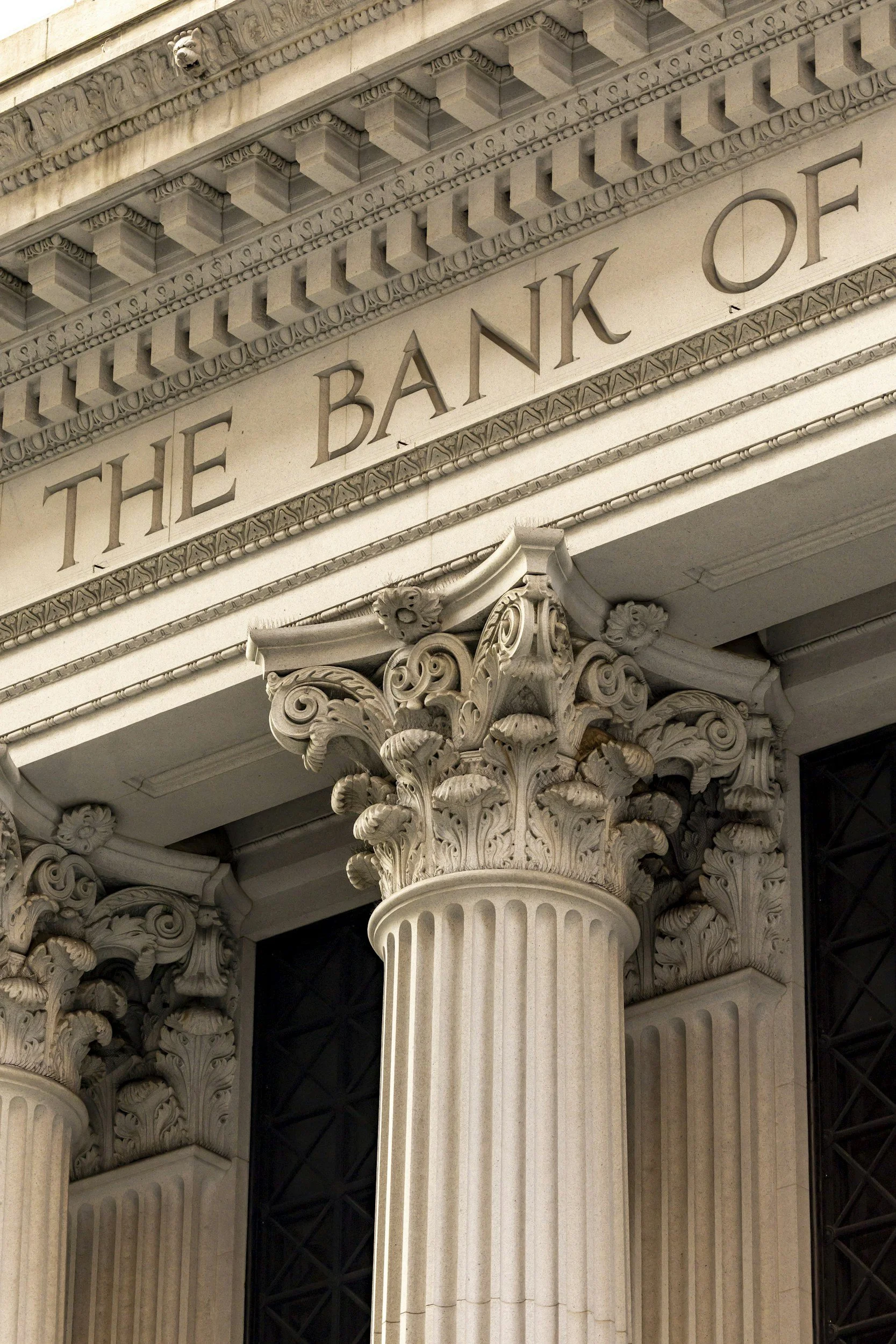 Close-up of the entrance of The Bank of America building, featuring classical architectural details including Corinthian columns, ornamental capitals, and a frieze with a lion head sculpture.
