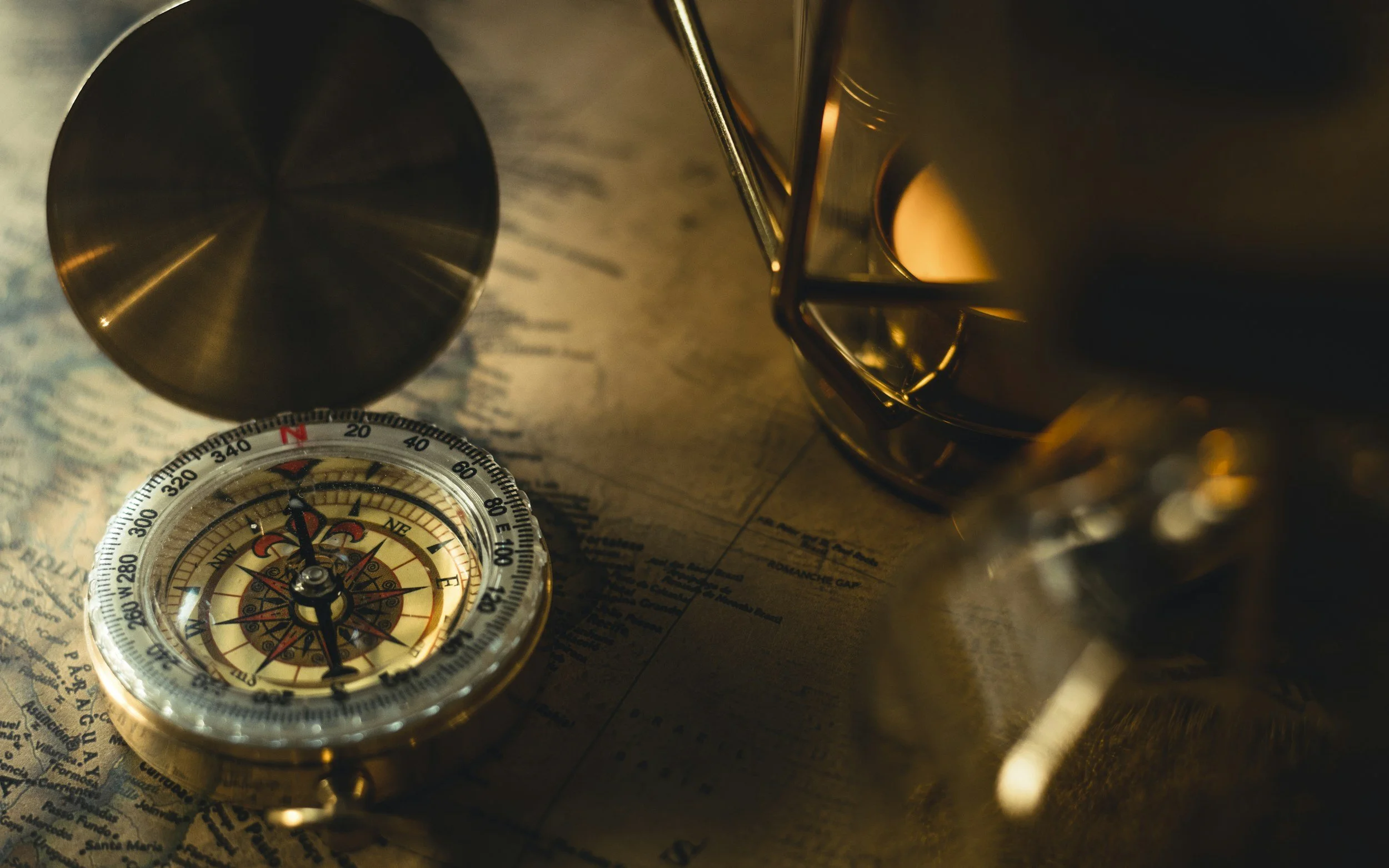 A close-up of a vintage compass, a metal cup, and a metal mug placed on an old map.