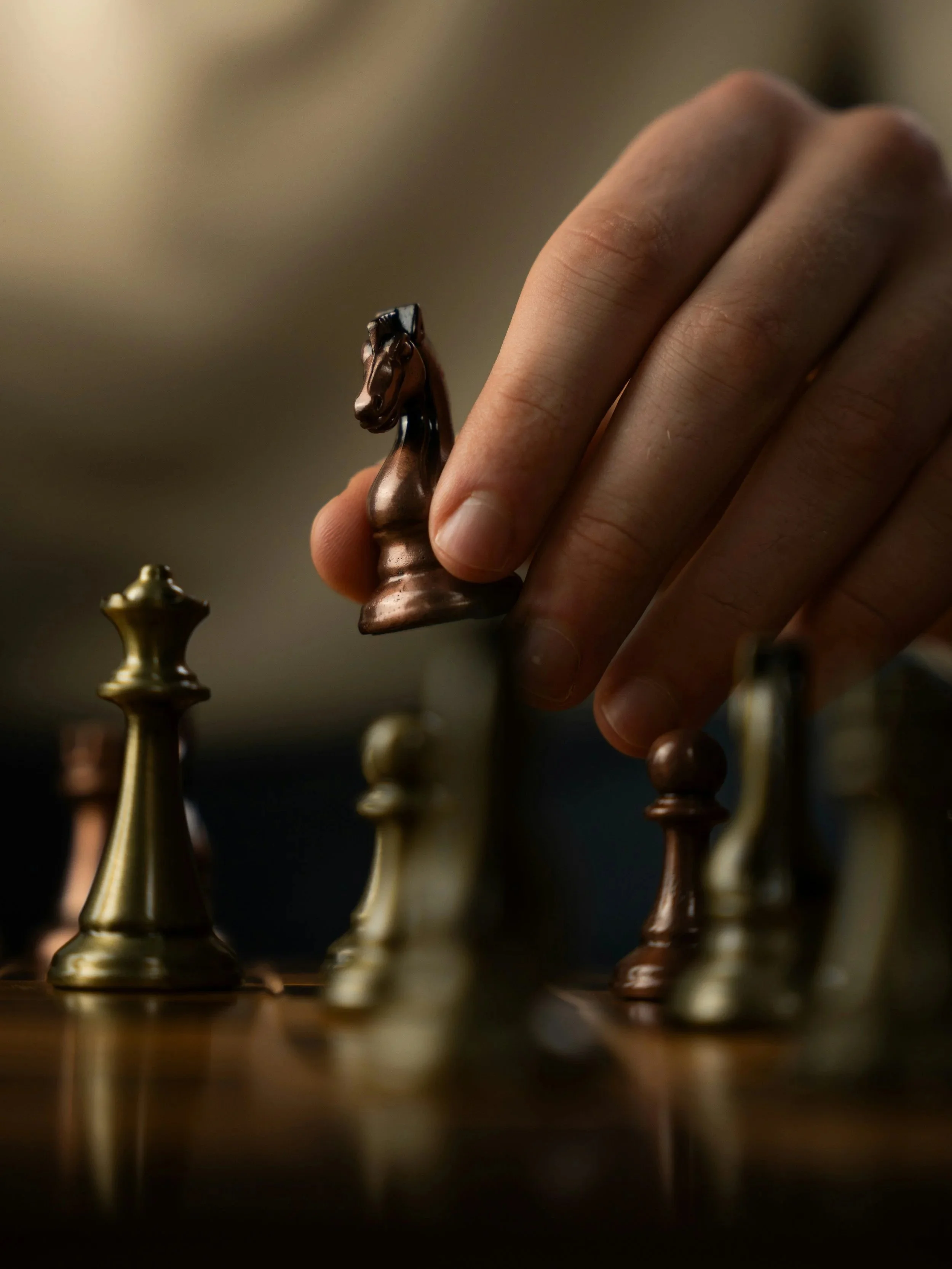 Close-up of a person's hand moving a black king chess piece on a chessboard, surrounded by other colored chess pieces.