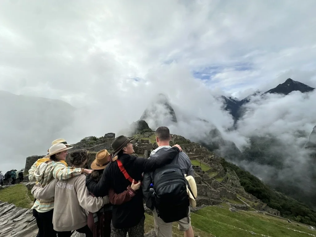 Tourists at Machu Picchu in cloudy weather with terraced ruins and mountains in the background.