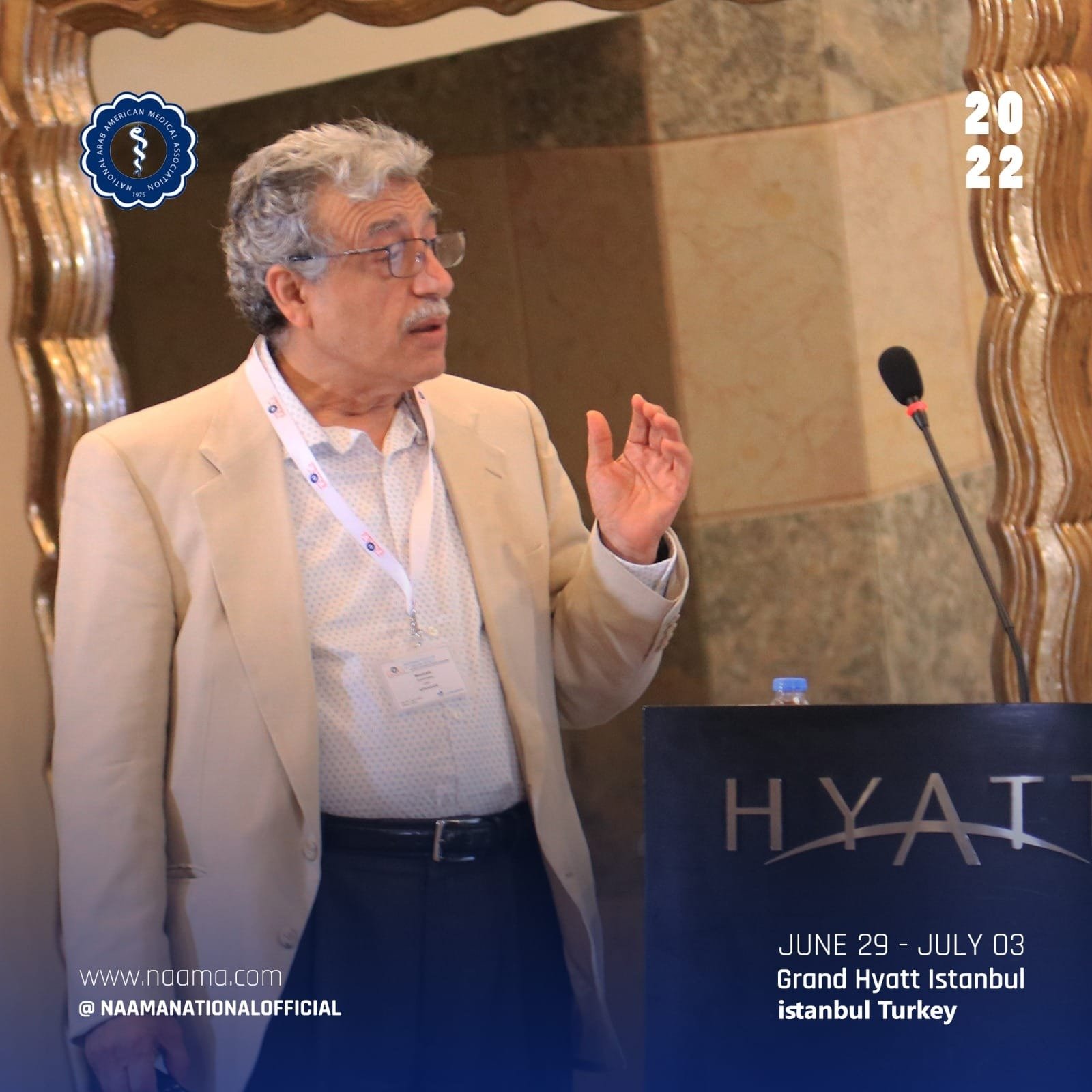 A man with gray hair and glasses wearing a beige blazer and white shirt speaking at a conference, standing behind a podium with 'HYATT' written on it, in a hotel conference room. The date and location are shown as June 29 - July 03 at the Grand Hyatt
