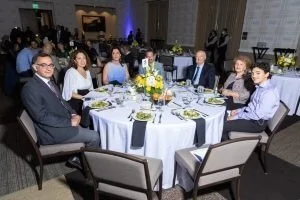 Group of eight people sitting around a round banquet table at a formal event.